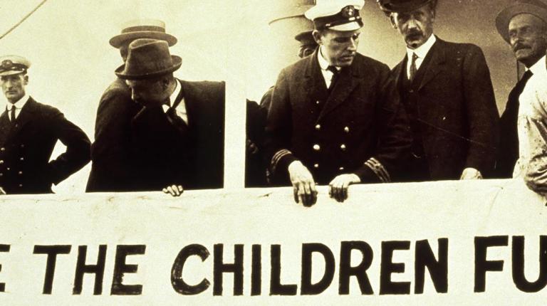 sailors standing behind save the children banner